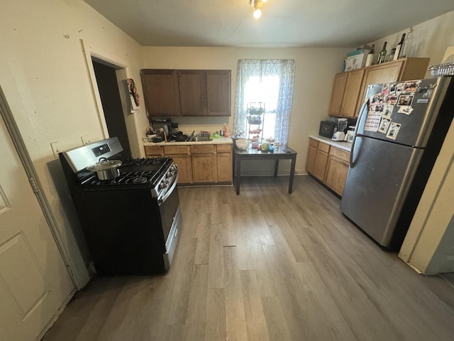 kitchen featuring appliances with stainless steel finishes, brown cabinetry, light countertops, and light wood-style flooring