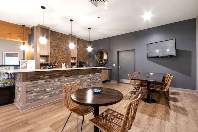 bar with a community bar, visible vents, baseboards, light wood-style flooring, and decorative light fixtures