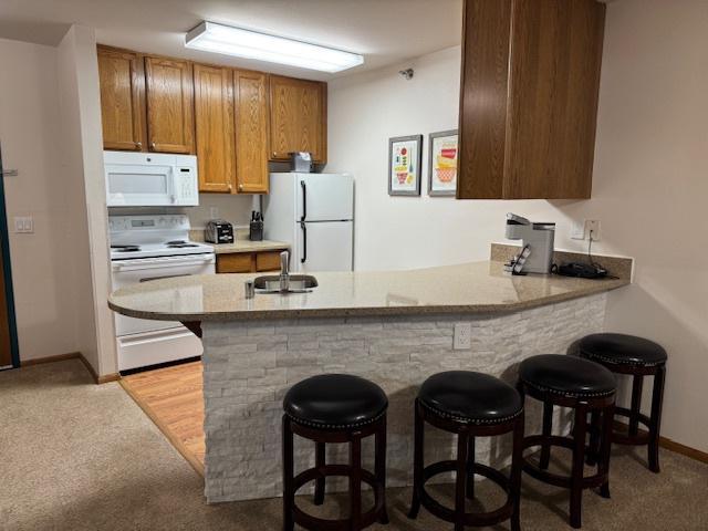 kitchen featuring a breakfast bar, white appliances, a sink, and a peninsula