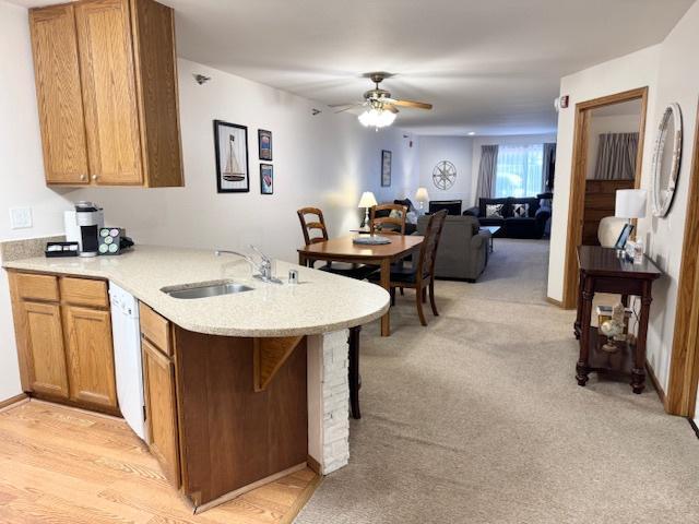 kitchen featuring light colored carpet, light countertops, white dishwasher, a sink, and a peninsula