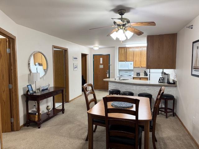 dining area with light carpet, a ceiling fan, and baseboards