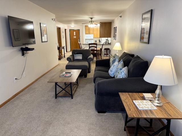 living room with light carpet, a ceiling fan, and baseboards