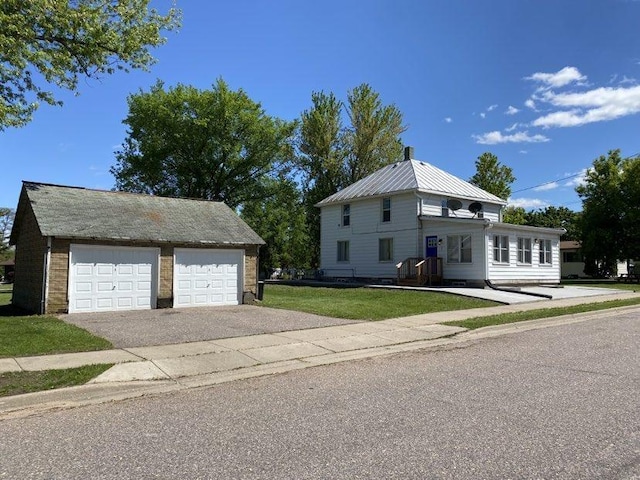 view of front facade featuring an outdoor structure, a front yard, a detached garage, and metal roof