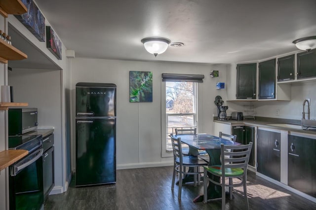 kitchen featuring stainless steel microwave, dark wood finished floors, light countertops, freestanding refrigerator, and a sink