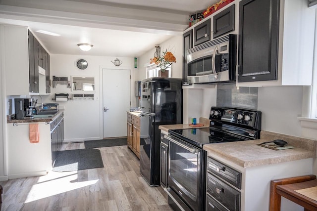 kitchen featuring backsplash, light countertops, light wood-style flooring, black appliances, and a sink