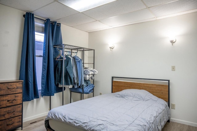 bedroom featuring a paneled ceiling, visible vents, baseboards, and wood finished floors