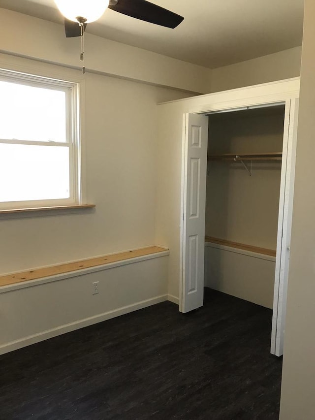 unfurnished bedroom featuring dark wood-style floors, a closet, baseboards, and a ceiling fan
