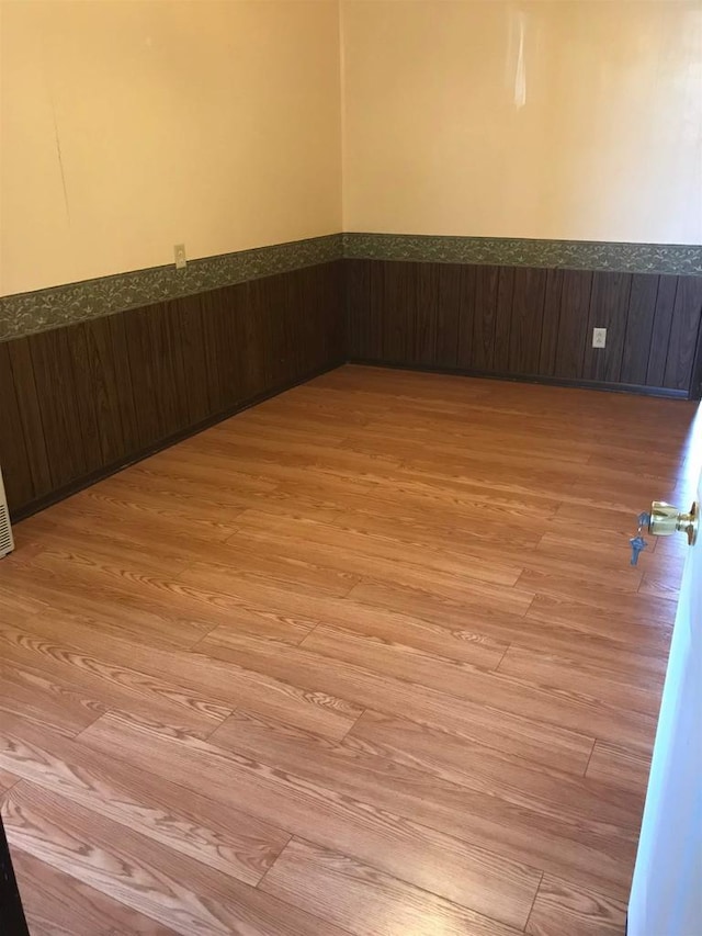 unfurnished room with light wood finished floors and wainscoting