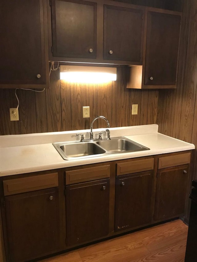 kitchen featuring light countertops, wood walls, a sink, and dark brown cabinetry