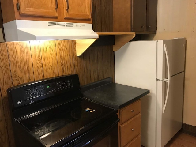 kitchen featuring black range with electric stovetop, brown cabinetry, exhaust hood, and freestanding refrigerator