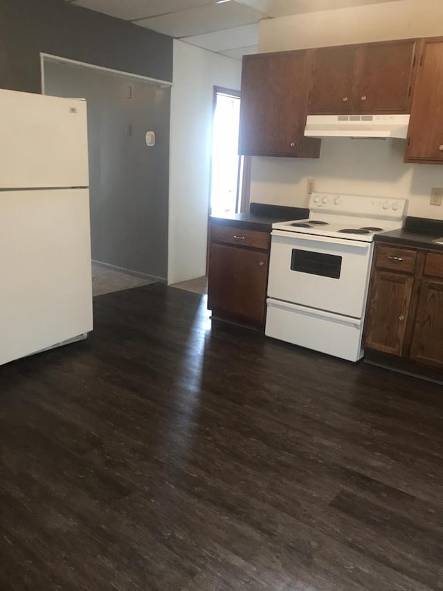 kitchen with dark wood-type flooring, dark countertops, white appliances, and under cabinet range hood