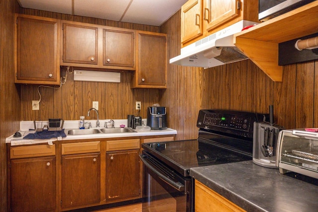 kitchen featuring brown cabinetry, a sink, under cabinet range hood, and black / electric stove