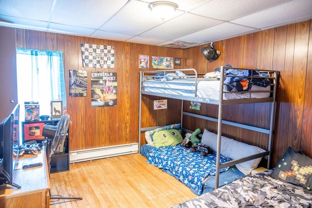 bedroom featuring wood-type flooring, a drop ceiling, wooden walls, and baseboard heating