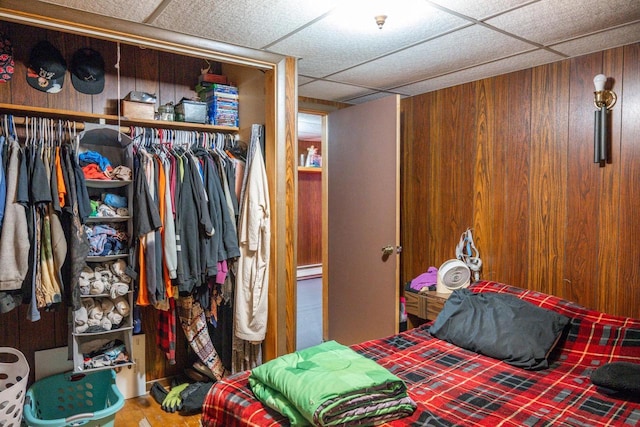 bedroom featuring a paneled ceiling, a closet, wood walls, and wood finished floors