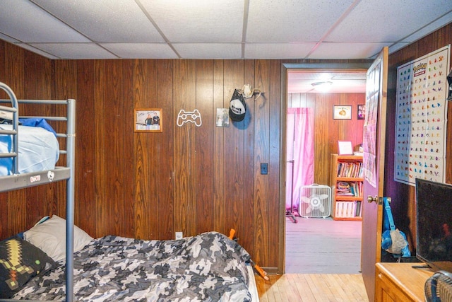 bedroom with wood walls, a drop ceiling, and wood finished floors