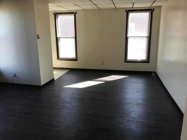 empty room with a paneled ceiling, baseboards, and wood finished floors