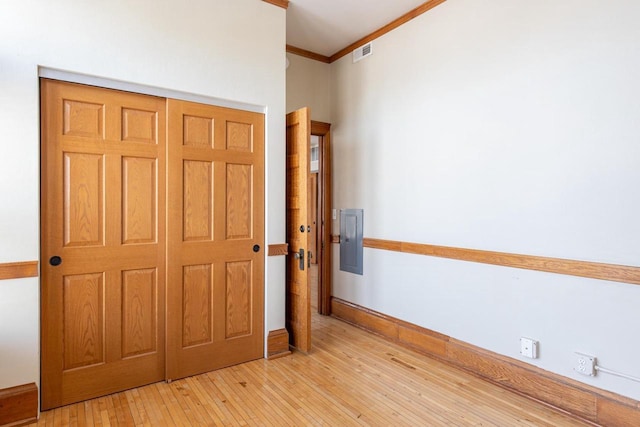 unfurnished bedroom with light wood finished floors, electric panel, baseboards, visible vents, and crown molding