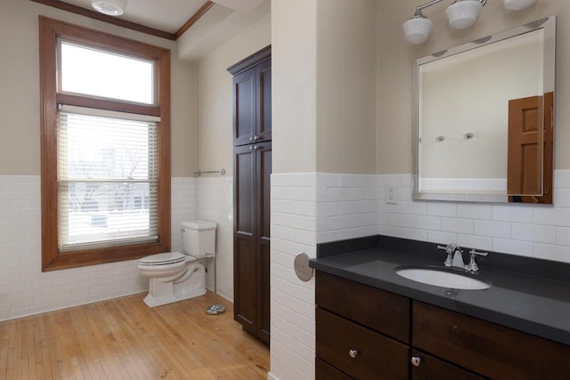 bathroom featuring toilet, a wainscoted wall, wood finished floors, vanity, and tile walls