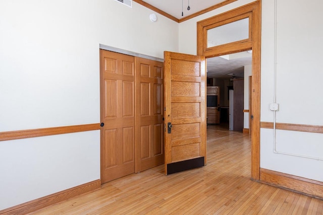 empty room featuring baseboards, ornamental molding, and light wood-style floors