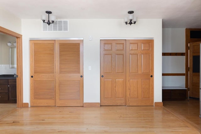 unfurnished bedroom with light wood-type flooring, visible vents, and multiple closets