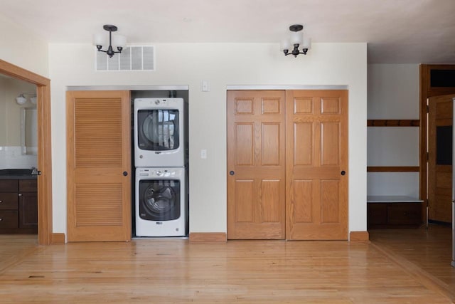 entrance foyer featuring a notable chandelier, stacked washer / dryer, visible vents, baseboards, and light wood finished floors