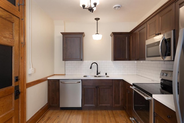 kitchen with light wood finished floors, light countertops, backsplash, appliances with stainless steel finishes, and a sink