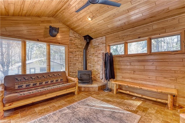 living room featuring ceiling fan, lofted ceiling, wooden ceiling, wood walls, and a wood stove