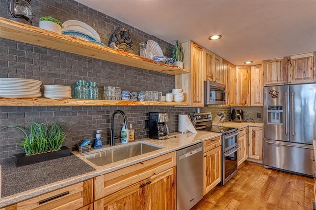 kitchen featuring light wood finished floors, open shelves, backsplash, appliances with stainless steel finishes, and a sink