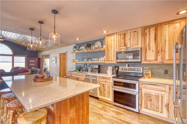 kitchen featuring light stone countertops, stainless steel appliances, light brown cabinetry, light wood-style floors, and a kitchen bar