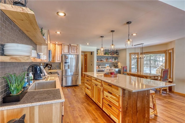 kitchen with light wood-style flooring, a breakfast bar, a sink, stainless steel fridge with ice dispenser, and open shelves