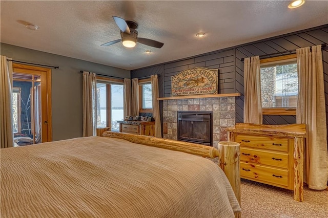 carpeted bedroom featuring ceiling fan, multiple windows, a textured ceiling, and a tile fireplace