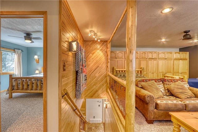 wine room featuring a ceiling fan, light colored carpet, wood walls, and a textured ceiling