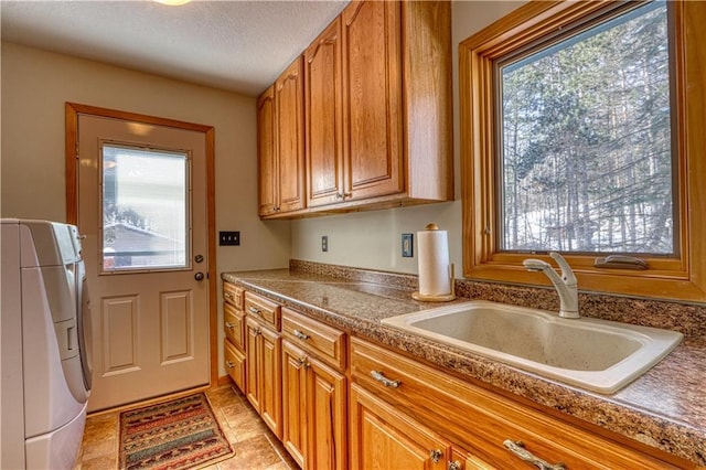 kitchen with washer / dryer, plenty of natural light, brown cabinetry, and a sink