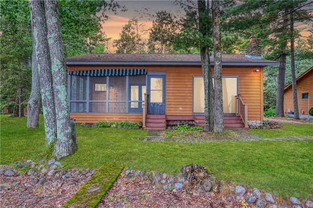 view of front facade featuring entry steps, a sunroom, a chimney, and a front yard