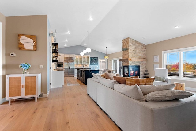 living room featuring lofted ceiling, a stone fireplace, light wood finished floors, and baseboards