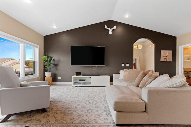 living area featuring arched walkways, an accent wall, lofted ceiling, and baseboards