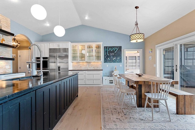 kitchen featuring arched walkways, stainless steel appliances, lofted ceiling, dark countertops, and a sink