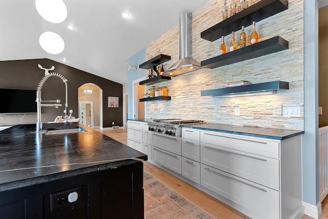 kitchen with arched walkways, decorative backsplash, dark countertops, stainless steel gas stovetop, and open shelves