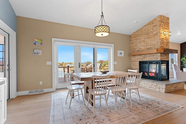 dining area featuring a fireplace, light wood finished floors, lofted ceiling, visible vents, and baseboards