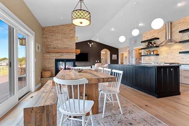 kitchen with light wood-type flooring, arched walkways, vaulted ceiling, and dark cabinets