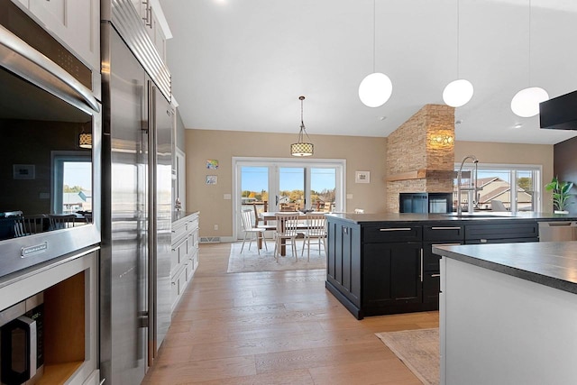 kitchen with a sink, appliances with stainless steel finishes, dark cabinetry, light wood-type flooring, and pendant lighting