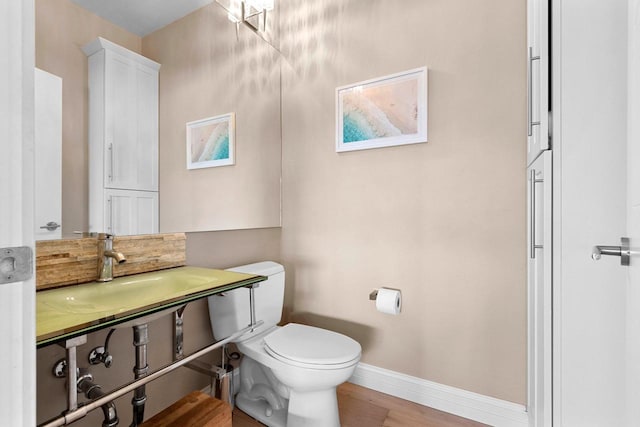 half bathroom featuring baseboards, a sink, toilet, and wood finished floors