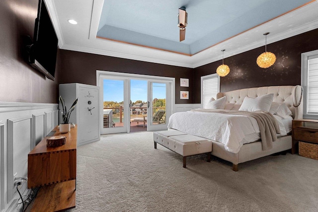 carpeted bedroom featuring a wainscoted wall, access to outside, a tray ceiling, crown molding, and a decorative wall
