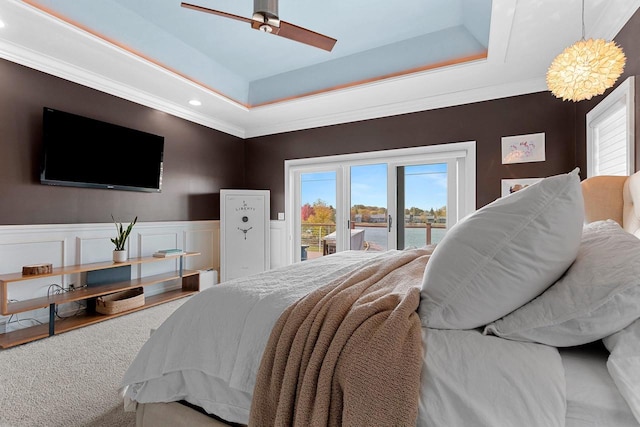 carpeted bedroom with access to exterior, multiple windows, a raised ceiling, and wainscoting