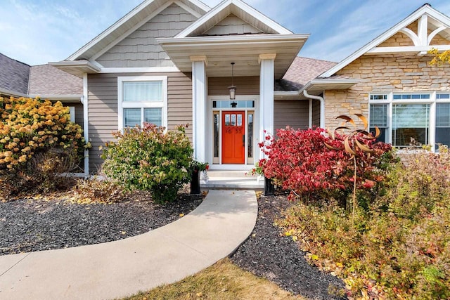 doorway to property featuring stone siding and roof with shingles