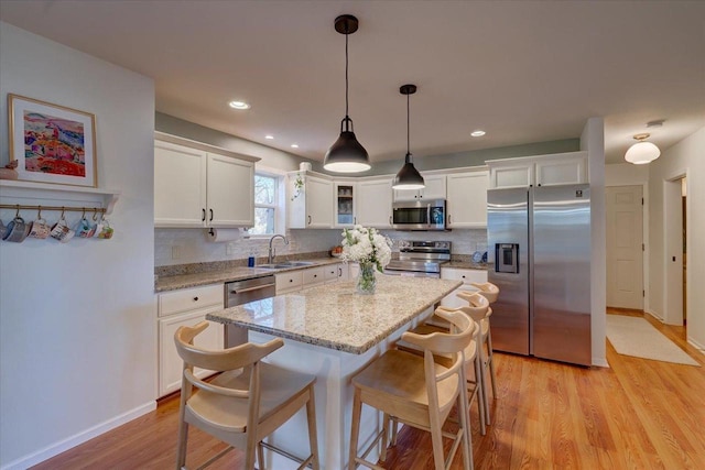 kitchen featuring a breakfast bar, a sink, tasteful backsplash, white cabinetry, and appliances with stainless steel finishes