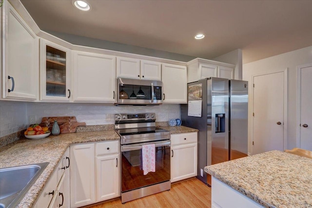 kitchen featuring a sink, tasteful backsplash, appliances with stainless steel finishes, white cabinets, and light wood finished floors