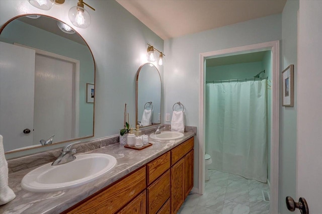 bathroom with double vanity, marble finish floor, toilet, and a sink