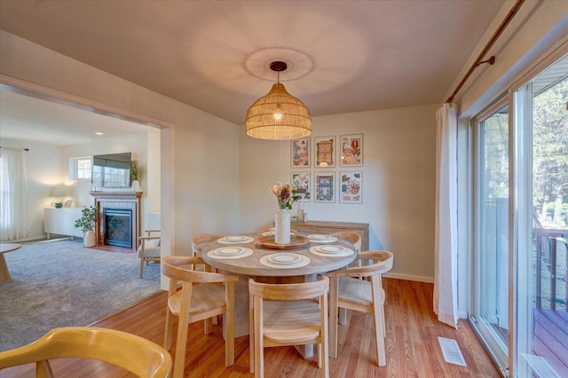 dining room featuring a fireplace with flush hearth, baseboards, visible vents, and light wood-type flooring