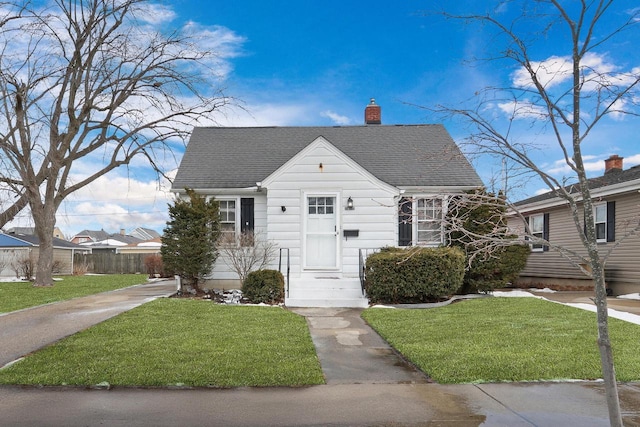 view of front of house featuring a shingled roof, a chimney, fence, and a front lawn